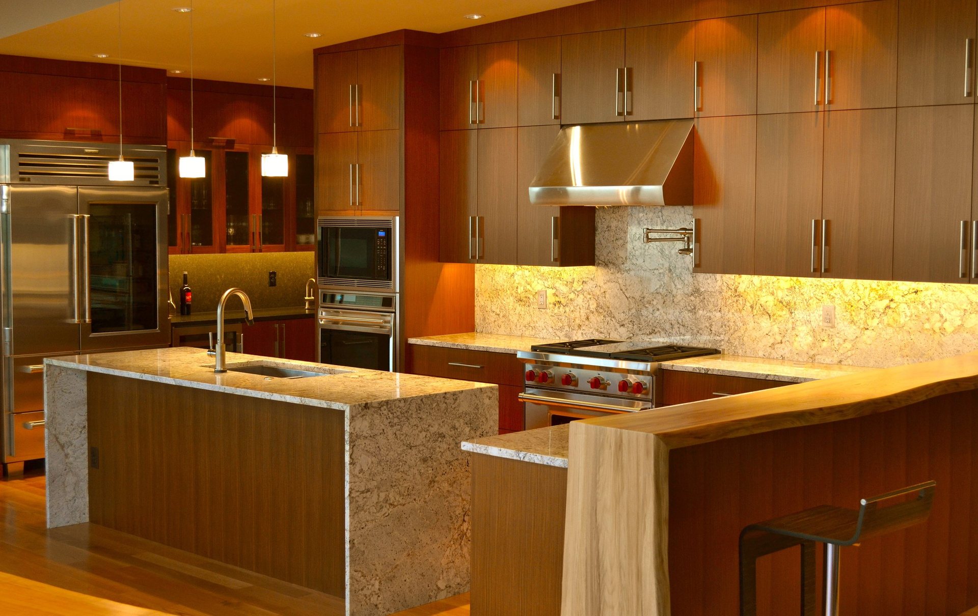 Afrormosia kitchen cabinetry with granite counters and a live-edge bar top under warm task lighting