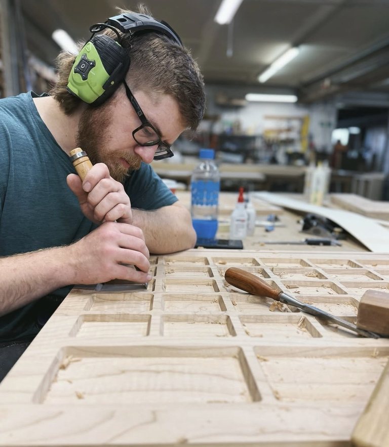 Madera craftsman hand-chiselling a coffered maple panel at the bench in the Tacoma studio