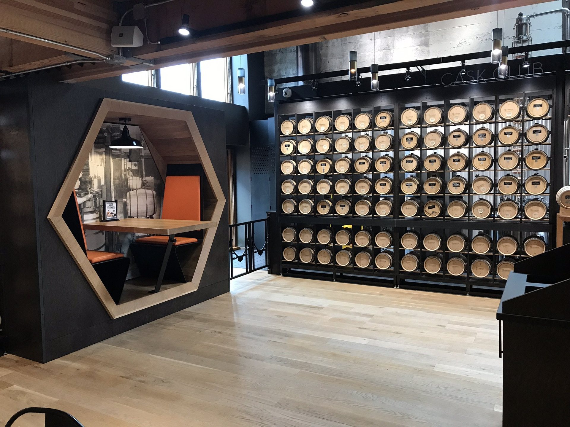 Distillery tasting room with a steel and oak cask wall and a hexagonal ash booth built to spec
