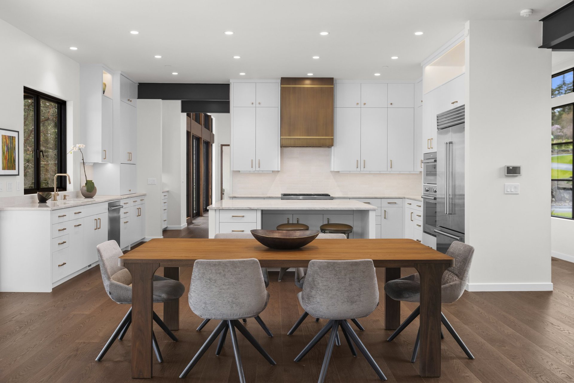 Custom white kitchen with a solid walnut dining table, brass range hood and brass cabinet hardware