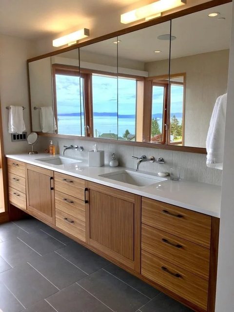 Floating teak double vanity with quartz counters and a full-width mirror cabinet framing a water view