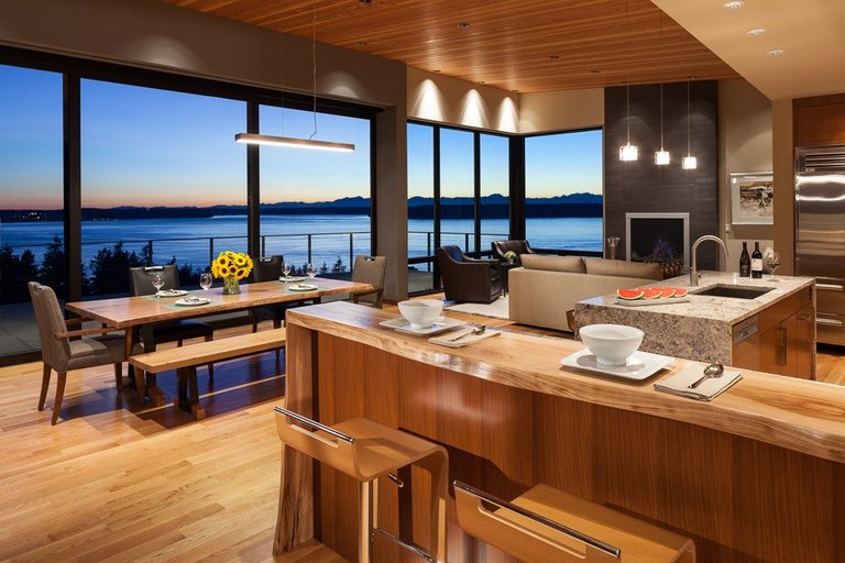 Waterfront kitchen at dusk with a live-edge wood bar counter and cedar ceiling above Puget Sound